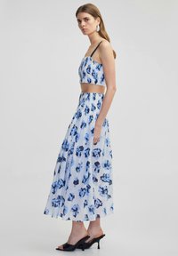 Dvoudílný outfit se světle modrým květinovým crop topem s tenkými ramínky a odpovídající maxi sukni s sklady, oba v odstínech modré a černé.