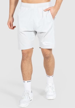 Man wearing white sports shorts with side pockets, white crew socks with black text, and white sneakers against plain background.