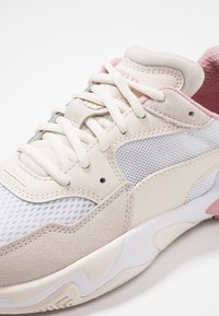 Sneaker w beżowo-różowym schemacie kolorystycznym, wykonany z siateczki i zamszu, o zaokrąglonym kształcie z wyraźnymi sznurówkami i teksturowanymi akcentami.