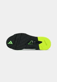 Semelle de chaussure de sport noire avec des accents verts. Motif de traction visible, avec un design triangulaire au niveau du talon et des surfaces de grip texturées.