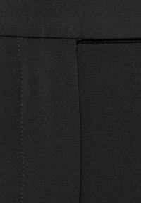Schwarzer Stoff mit glatter Textur, der eine genähte Naht und eine kleine Tasche aufweist. Das Material wirkt strapazierfähig und leicht dehnbar.