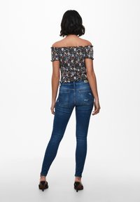 Floraalinen olkaimeton paita, jossa on röyhelöhihoja; yhdistettynä tummansinisiin slim fit -farkkuihin, joissa on kulutettu muotoilu ja takataskut.