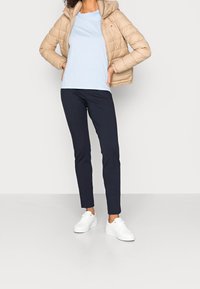 Chaqueta acolchada beige con capucha, camiseta azul clara, pantalones azul marino y zapatillas blancas. Texturas suaves y diseño ajustado con costuras laterales.