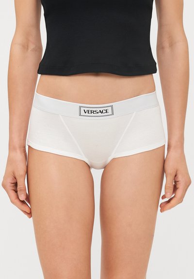 Pantalones cortos de algodón blanco con una textura suave, que cuentan con una amplia cinturilla elástica etiquetada como "VERSACE". El diseño tiene un corte clásico ajustado.