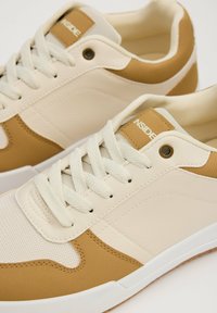 Zapatillas con un diseño en cuero crema y gamuza marrón, paneles de malla texturizada, cordones blancos y suelas de goma. Acabadas con detalles de la marca.