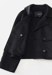 Cappotto nero corto realizzato in tessuto morbido, dotato di colletto a revers, chiusura doppiopetto e sottili dettagli con bottoni.