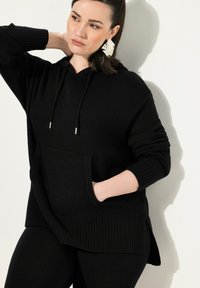 Felpa nera con cappuccio realizzata in tessuto texturizzato, caratterizzata da una tasca frontale, polsini a costine e spacchi laterali per un tocco aggiuntivo.