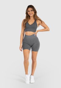 Ensemble de sport gris comprenant un top court à col en V et un short taille haute assorti, fabriqué en tissu extensible. Des baskets blanches viennent parfaire le look.