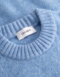 Ljusblå stickad tröja med ribbat rundhals och en vit etikett med texten "LES DEUX" sydd inuti kragen.