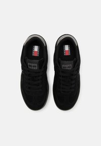 Baskets en suède noir avec une finition lisse, dotées de lacets noirs plats, de détails perforés et d'une languette de marque avec des accents rouges, blancs et bleus.