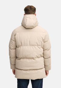 Chaqueta de plumas en beige claro con un acabado texturizado, que presenta una capucha, un diseño de paneles y un dobladillo ligeramente alargado en la parte posterior.