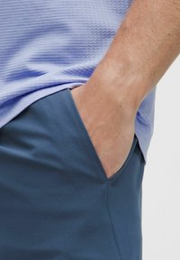 Šviesiai purpurinė marškinėliai su tekstūruotu raštu, derinami su tamsiai mėlynomis šortais, turinčiais šoninį kišenį. Audinys atrodo lygus ir lengvas.