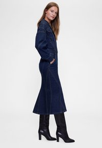 Tumesinises toonis teksakleit, millel on kehasse tõmmatud ülaosa, lehviva lõikega alumine osa ja kontrastsed õmblused. Komplekteeritud kõrgete mustade nahkkingadega.