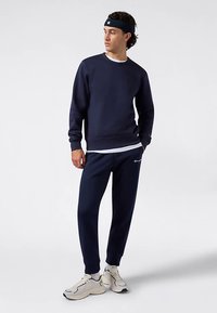 Navy sweatshirt with a crew neckline, paired with navy pants. Both made of cotton, featuring a white accent shirt underneath. Light-colored sneakers.