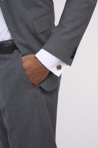 Grau maßgeschneiderter Anzug mit strukturiertem Finish, ergänzt durch ein weißes Hemd mit runden metallischen Manschettenknöpfen und schwarzen Knöpfen.