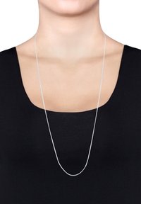 Sølv kædehalssmykke, slankt, afrundet form. Det hænger glat over en sort top, med en fin tekstur og minimale design detaljer.