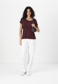 T-shirt à imprimé léopard rouge et noir à manches courtes, associé à un pantalon large blanc et des baskets blanches, portant un petit sac noir.