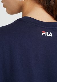 Zbliżenie na ramię osoby w granatowej koszulce FILA, z logo nadrukowanym w okolicy dekoltu z tyłu.