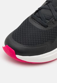 Černá sportovní bota s texturovaným látkovým svrškem, gumovou špičkou a výrazně růžovou podešví. Bílé akcenty na mezipodešvi vytvářejí kontrast.