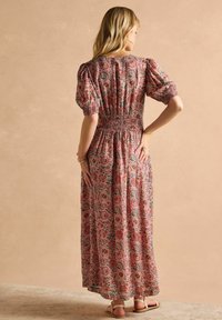 Maxikleid mit floralen Motiven in Pink mit grünen Akzenten, gerafftem Brustbereich, Puffärmeln und einem fließenden, strukturierten Stoff. Sandalen runden das Outfit ab.