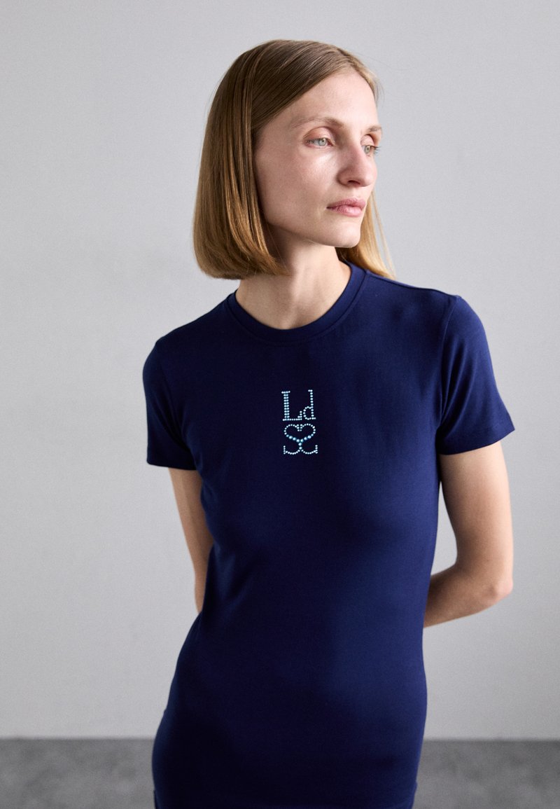 Navy blue fitted t-shirt in cotton blend with short sleeves. Features small rhinestone logo at chest. Smooth texture, classic crew neck design.