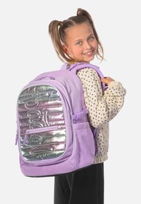 Fioletowy plecak z błyszczącym srebrnym panelem przednim, podwójnymi zamkami błyskawicznymi, regulowanymi paskami i teksturowanym materiałem. Akcentowany refleksami światła.