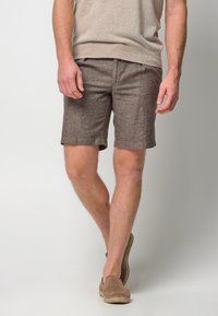 Light brown linen shorts with a subtle texture, featuring a mid-rise waist and two front pockets. Paired with beige slip-on shoes.