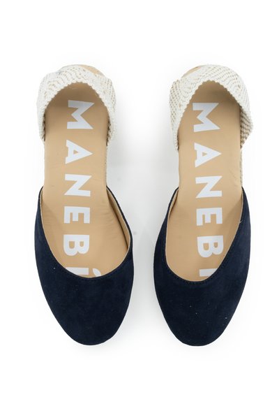 Marineblaue Wildleder-Slipper mit einem gewebten beigen Riemen, ausgestattet mit einem glatten Innenleben und dem Markennamen in Weiß auf der Einlegesohle gedruckt.