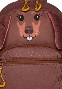 Mochila temática de perro marrón con diseño de cara de perro caricaturesca, acentos suaves en las orejas, superficie texturizada y un bolsillo delantero con cremallera.