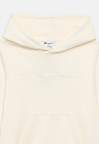 Φούτερ τύπου μπλούζα με κουκούλα σε εκρού απόχρωση, με κεντημένο λογότυπο "Champion". Διαθέτει μπροστινή τσέπη και κουκούλα με κορδόνι, κατασκευασμένο από απαλό ύφασμα.