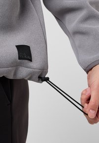 Felpa grigia in tessuto testurizzato, con un patch del logo nero di Jack Wolfskin e lacci regolabili all'orlo.