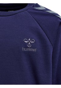 Sweatshirt bleu marine avec des manches raglan, présentant un motif texturé sur les épaules et un logo brodé en argent sur la poitrine.
