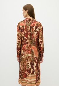 Langärmeliges Hemdkleid mit einem bunten Paisleymuster in erdigen Tönen. Verfügt über einen gefütterten Kragen und geknöpfte Manschetten sowie einen gestreiften Saum.