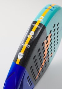 Racchetta da padel a forma di goccia con superficie nera, dettagli in teal e accenti arancioni. Include materiali in fibra di carbonio e un branding specifico.