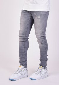Jeans skinny in denim grigio con dettagli strappati, abbinati a sneakers bianche e grigie con accenti blu e suola testurizzata.