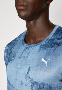 Blauw, gewatteerd shirt met korte mouwen, ronde halslijn en een wit Puma-logo op de borst. De stof toont een subtiele patroonverloop.