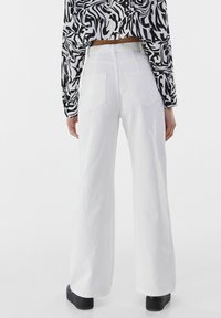 Jeans anchos blancos de talle alto con grandes bolsillos traseros, combinados con un top corto de patrón en blanco y negro. Zapatos de plataforma negros visibles.