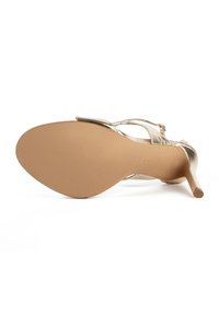 Gouden metallic hoge hak sandaal met een strakke vormgeving, voorzien van een gladde textuur, smalle bandjes en een puntige neus. Lichtbruine zool.