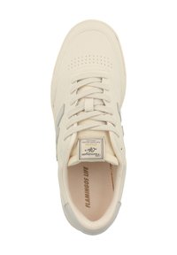 Cream-colored sneaker with perforated toe, textured fabric, flat laces, and subtle gray accents. Features a logo tag on the tongue.