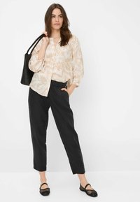 Lichtbeige bloemenshirt met losse mouwen, gecombineerd met zwarte, losse broek. Een zwarte tote bag en mesh zwarte flats maken de outfit compleet.