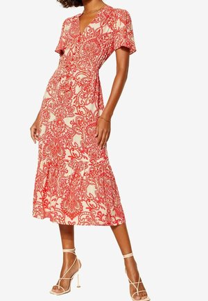 Woman wearing a mid-length cream dress with red floral patterns, short sleeves, and beige strappy high-heeled sandals.