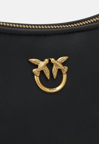Sac en cuir noir avec une bague dorée ornée de deux accents d'oiseaux décoratifs. Détail de fermeture éclair sur le dessus. Surface texturée.
