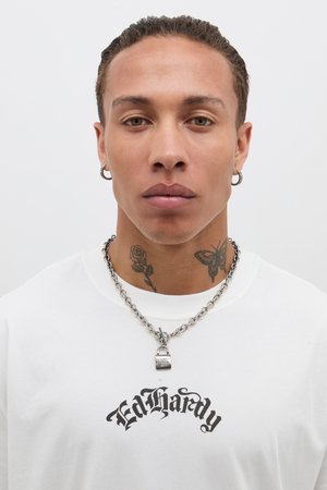 Maglietta bianca con il logo nero "Ed Hardy", collana in argento e pendant a forma di lucchetto. Presenta tatuaggi di una rosa e una farfalla sul collo.