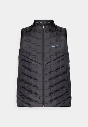 Fekete puffermellény magas gallérral, elülső cipzárral és oldalsó zsebekkel. Varrott mintákkal és kék Nike logóval a mellkason.