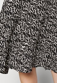 Jupe à motifs noirs et blancs avec un design fluide, dotée d'une taille froncée et d'un tissu texturé, présentant des formes abstraites irrégulières.