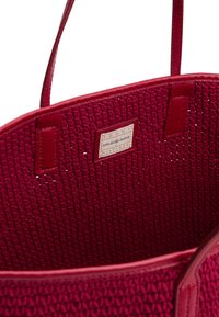 Borsa a mano rossa intrecciata realizzata in materiale testurizzato con dettagli in pelle. L'interno presenta un'etichetta, design aperto nella parte superiore e manici robusti.