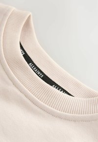 Helles beiges Crewneck-T-Shirt mit geripptem Kragen, ausgestattet mit einem schwarzen Etikett mit dem Text "AllSaints" entlang des inneren Halsausschnitts. Glatte Textur.