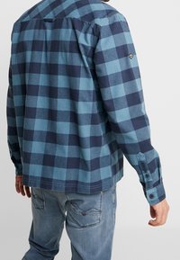 Camicia a quadri blu e navy realizzata in morbido tessuto, con chiusura a bottoni sul davanti, maniche lunghe e orlo dritto.