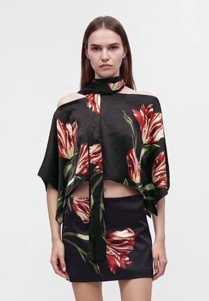 Femme portant un haut noir fleuri à épaules dénudées avec une écharpe assortie et une mini-jupe, avec de grands imprimés de tulipes rouges et blanches.