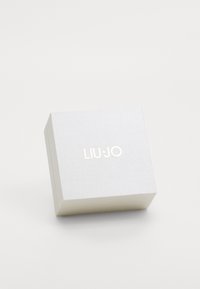 Cutie pătrată argintie cu o suprafață texturată, având un logo auriu "LIU·JO" în partea de sus. Design compact cu margini ascuțite.